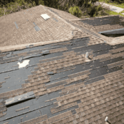 The image displays significant storm damage to a roof, characterized by missing and peeling shingles, exposing the underlying roofing materials.